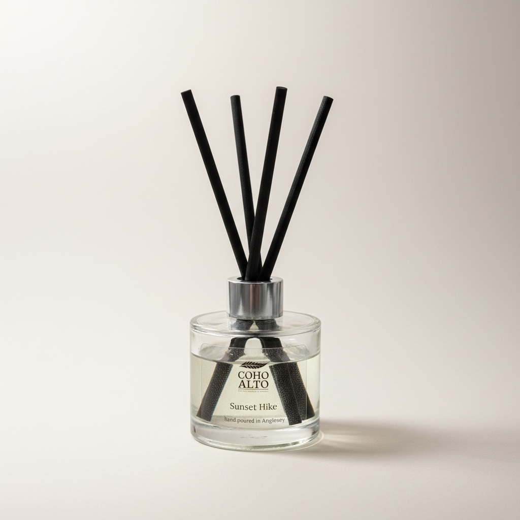 Reed diffuser with black sticks in a clear bottle labeled 'Coho Alto' on a light background