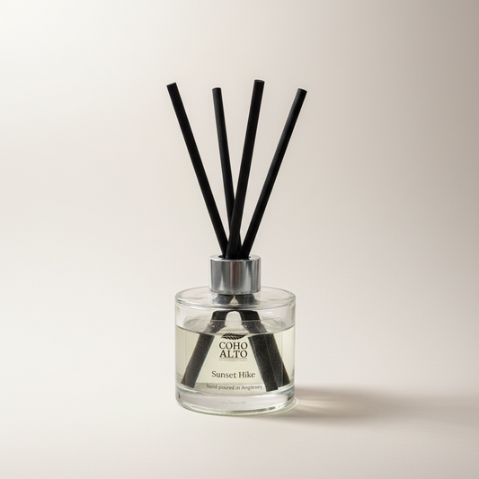 Reed diffuser with black sticks in a clear bottle labeled 'Coho Alto' on a light background